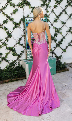 A woman in the Portia and Scarlett XO157 long formal dress, featuring a pink crystal-embellished bodice and beaded sheer back, stands outdoors by a tiled fountain and vine-covered wall.