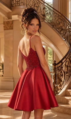 A woman wears the Beaded-Bodice Short A-Line Homecoming Dress XR6008, featuring a red, sleeveless design with a beaded bodice, as she stands before an ornate staircase in a grand, sunlit interior.