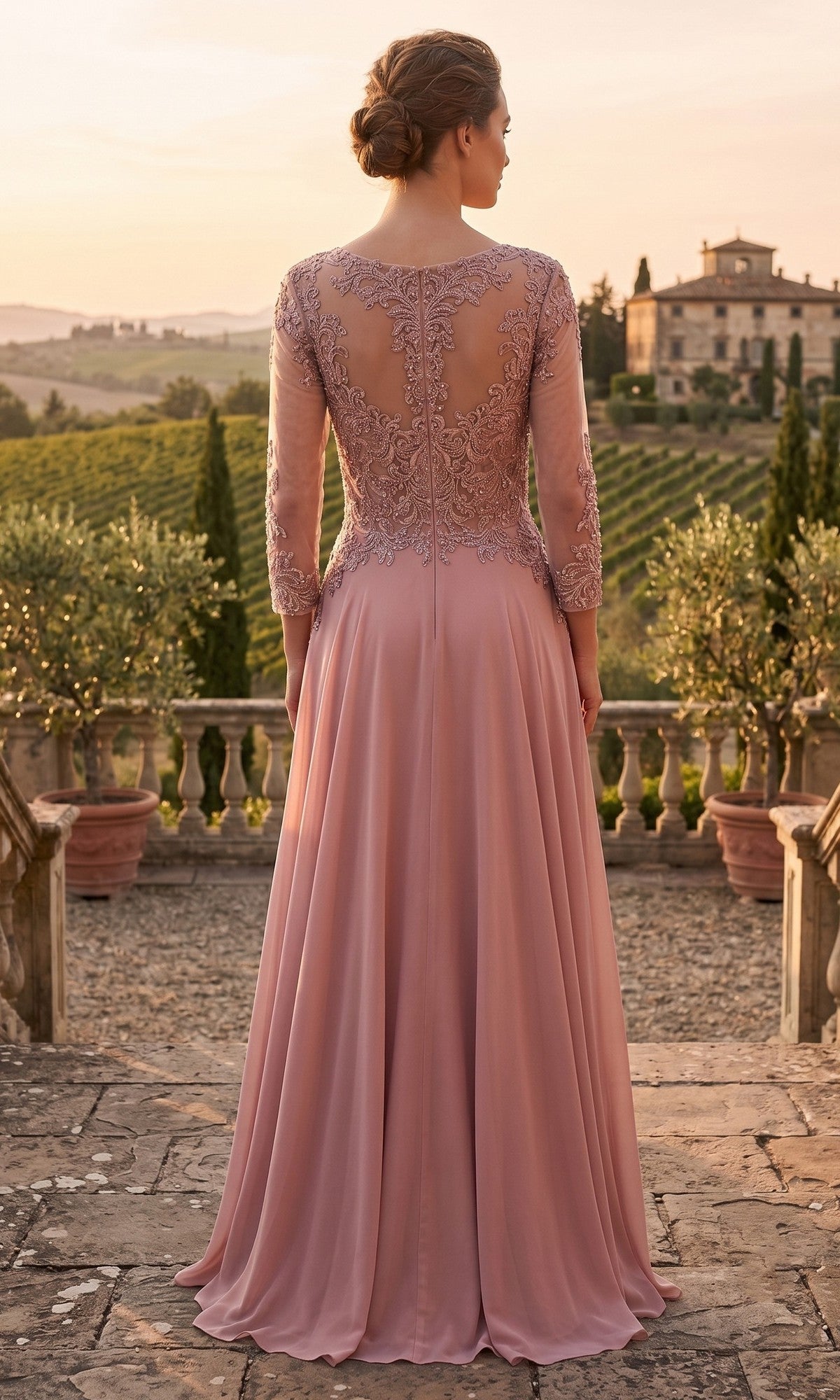 A woman with a low bun stands on a stone terrace overlooking a vineyard at sunset, wearing the Chicas XR6014 long prom dress—a mauve gown featuring an embellished bodice and delicate lace detailing on the back.