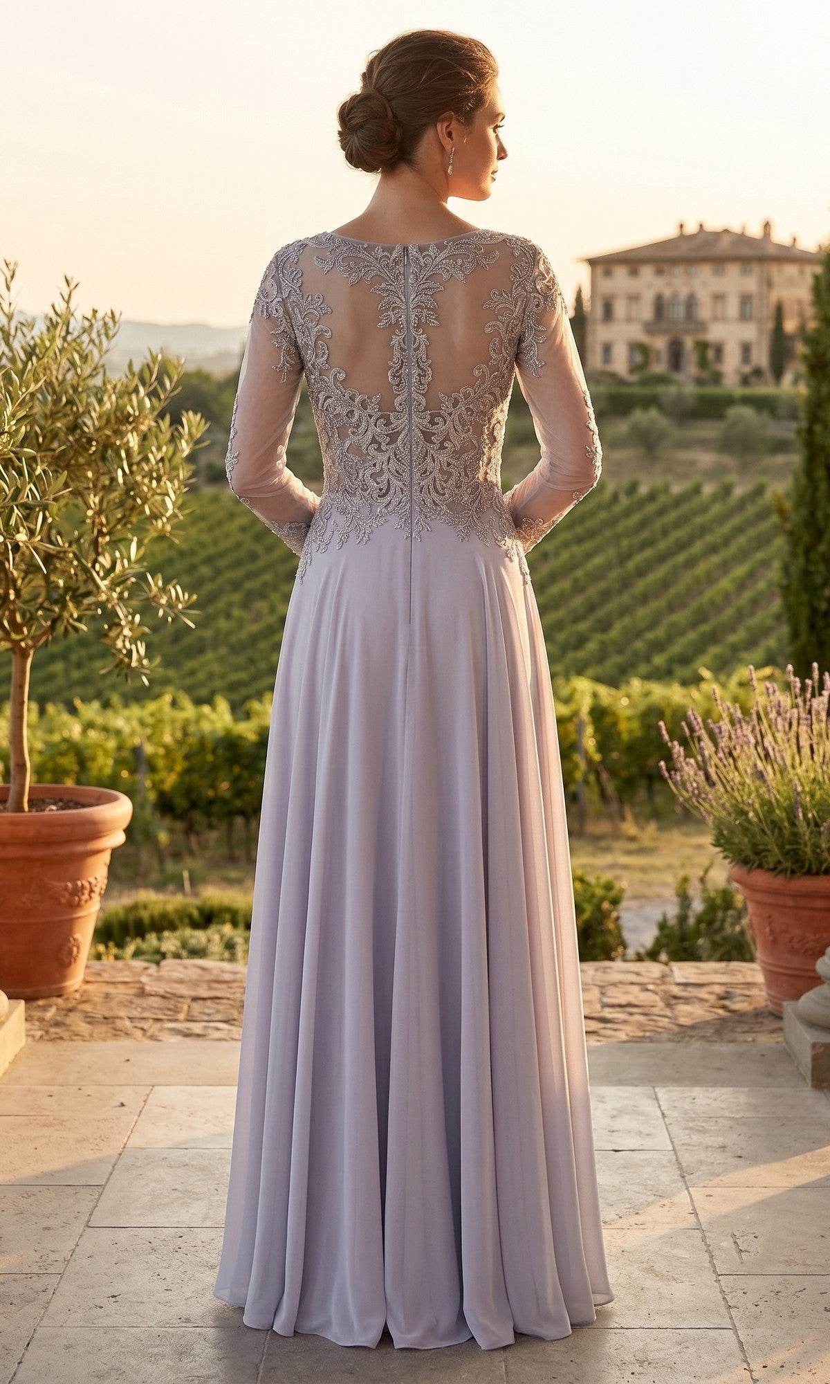 A woman stands outdoors overlooking vineyards at sunset, wearing the Long Prom Dress: Chicas XR6014—a lavender gown with a flowing chiffon skirt and a sheer lace back.