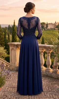 A woman in the Long Prom Dress: Chicas XR6014, a navy blue, floor-length gown featuring an embellished bodice and delicate lace detailing, stands on a terrace overlooking a scenic landscape at sunset.