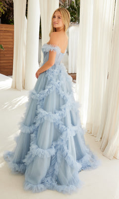 A woman stands indoors on a white floor, looking over her shoulder, wearing the Sheer-Waist Off-Shoulder Long Prom Ball Gown Y1472 in light blue with ruffled tulle. Sunlight filters through white curtains behind her.