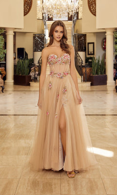 A woman stands indoors wearing the Nox Anabel Y1803 long champagne prom dress, featuring a strapless design, floral embroidery, and a thigh-high slit, with a chandelier and decorative columns in the background.