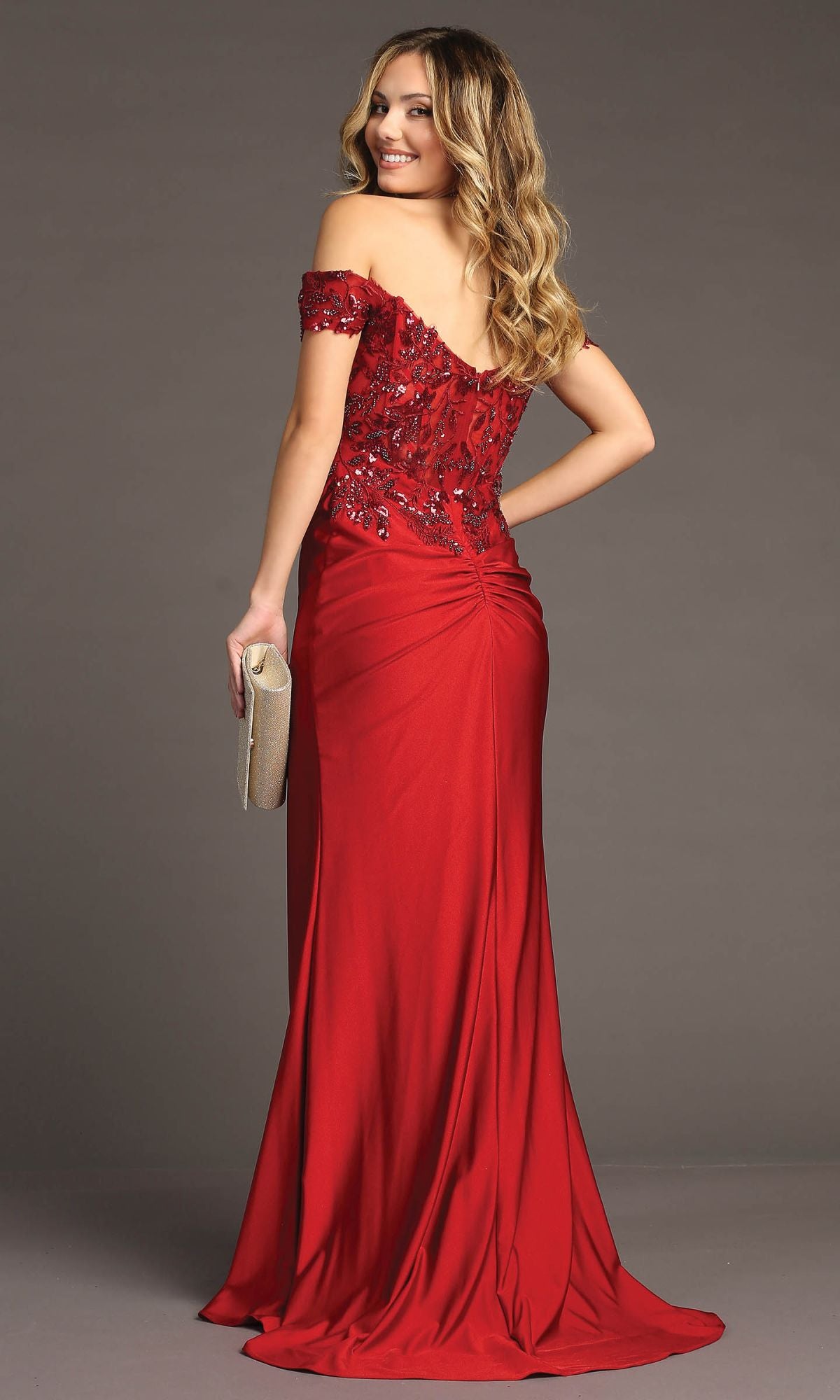 A woman in the Sequin-Bodice Long Prom Dress: Chicas YG5027, featuring an off-the-shoulder neckline, sequin corset bodice, and ruched back detail, holds a beige clutch against a plain background.