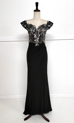 The Sequin-Bodice Long Prom Dress (Chicas YG5027) features a black sequin corset bodice, silver floral embroidered cap sleeves, and a floor-length skirt, displayed on a dress form.