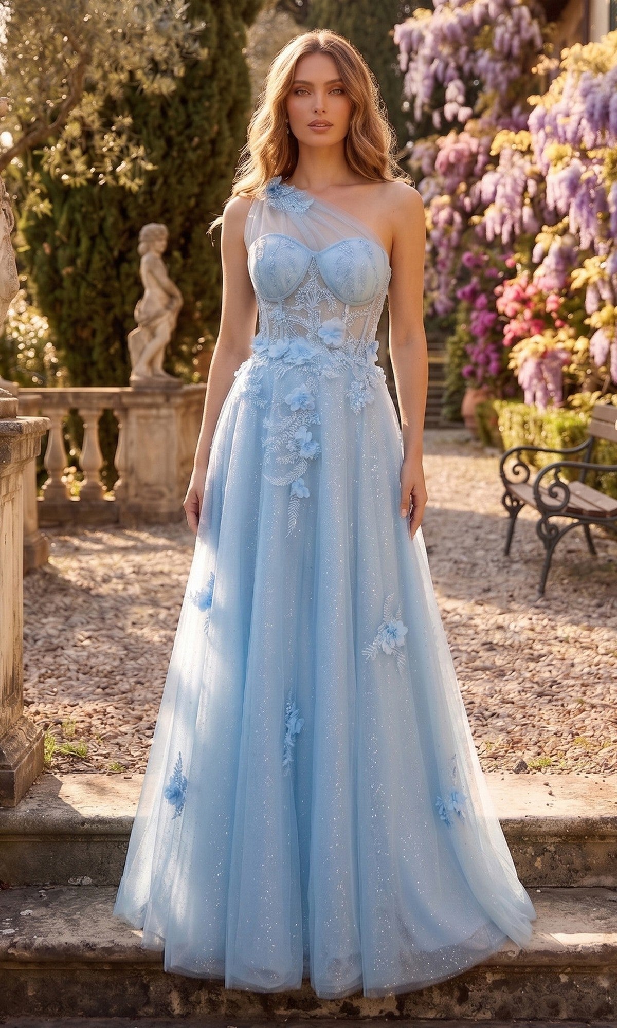A woman stands outdoors in a garden adorned with blooming flowers and statues, wearing the Chicas YG5028 long prom dress in baby blue—a floor-length, one-shoulder gown featuring floral appliqués and an elegant glitter tulle A-line skirt.