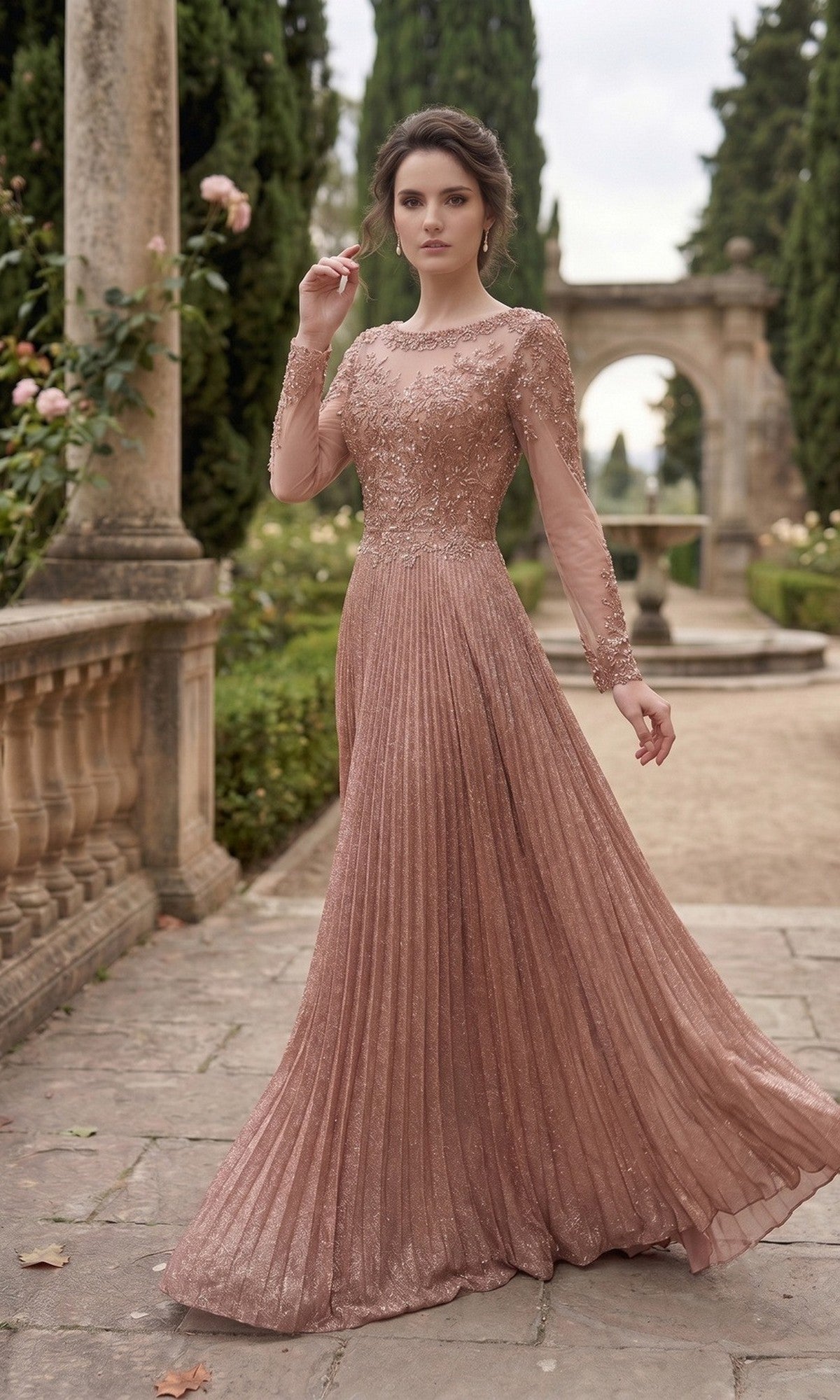 A woman stands outdoors in a modest Chicas YG5031 long formal dress—a flowing rose gown with pleats, sheer sleeves, and floral details. She is posed on a stone pathway surrounded by greenery and classical columns.