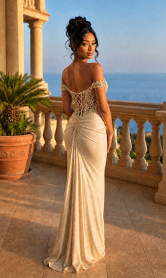 A woman in the Long Formal Dress: Chicas YG5037—an elegant, off-the-shoulder glitter gown with a beaded corset bodice—stands on a stone balcony with columns, gazing at the ocean during sunset.