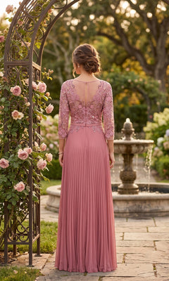 Wearing the Long Formal Dress: Chicas YG5038, a person stands with their back to the camera in a garden by a fountain and blooming roses. The dress features mauve lace, pleats, and an embroidered bodice for a modest formal look.