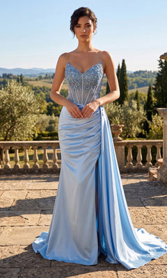 A woman stands outdoors wearing the Long Prom Dress: Chicas YG5041, a light blue, strapless gown adorned with beadwork and featuring a sheer bodice and high slit, set against a scenic landscape with a stone railing in the background.