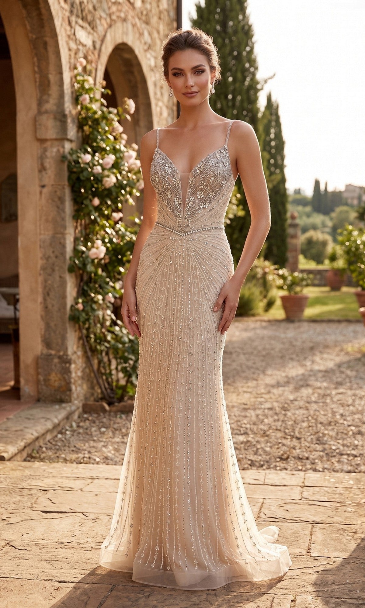 A woman in the Chicas YG5043 long prom dress in champagne, featuring a sleeveless design, sparkly fabric, floor-length silhouette, and deep V-neckline, stands outdoors on a stone patio near a building adorned with climbing roses.