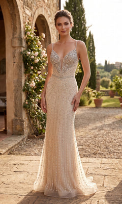 A woman in the Chicas YG5043 long prom dress in champagne, featuring a sleeveless design, sparkly fabric, floor-length silhouette, and deep V-neckline, stands outdoors on a stone patio near a building adorned with climbing roses.