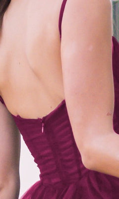 A person seen from behind wears the Sheer-Corset Long Prom Ball Gown: Yasmin by Velvi, a sleeveless burgundy dress with a sheer corset bodice and low back, revealing their upper back and part of one arm.