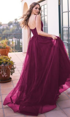 A woman in the Sheer-Corset Long Prom Ball Gown: Yasmin by Velvi, a sleeveless, floor-length tulle gown, stands on a tiled balcony holding her dress and looking over her shoulder.