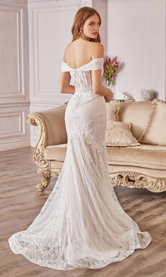 A woman wearing an Off-the-Shoulder Long White Lace Prom Gown stands before a beige ornate sofa in an elegant room with wood floors and decorative wall panels.