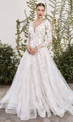 A woman wearing the Andrea and Leo A1067WC long formal dress, featuring elegant long sleeves and white floral lace appliques, stands outdoors in front of a vine-covered wall.