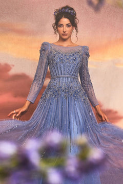 A woman in the Luxurious Formal Gown A1167 by Andrea and Leo, with sheer beaded details, poses against a pastel backdrop with purple flowers in the foreground.