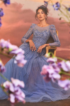 A woman in the Luxurious Formal Gown A1167 by Andrea and Leo sits on a gold chair, with blurred purple flowers around her against a warm background.