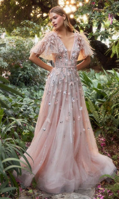 A woman stands in a garden wearing the Blush Pink Long Flutter-Sleeve Prom Gown A1176, featuring sheer sleeves, floral embellishments, and a deep V-neckline.