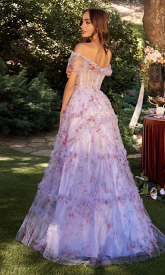 Outdoors, a woman looks over her shoulder in the Andrea & Leo A1286 long purple print prom dress. The off-the-shoulder gown's floral pattern and elegant design create a graceful, enchanting appearance.