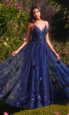A woman stands outdoors wearing the Andrea and Leo A1326, a navy blue floor-length glitter prom ball gown with floral appliqué, thin straps, and a flowing tulle skirt in an elegant A-line silhouette.