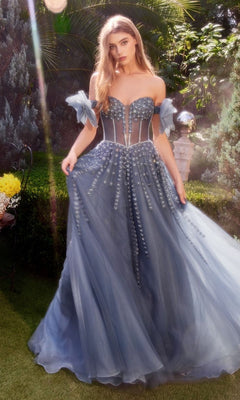 A woman in a strapless Andrea and Leo A1338 long prom dress stands on grass in a sunlit garden, gracefully holding the sides of her beaded evening gown.