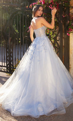 Wearing the Pastel Blue Ball Gown A1339 by Andrea and Leo, a woman stands outdoors near a black iron gate, turning to look over her shoulder.