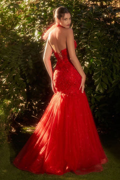 A woman stands outdoors before green foliage, looking over her shoulder in the Red Prom Dress A1345 by Andrea and Leo—featuring a fitted bodice, lace-up back, and flared tulle skirt.