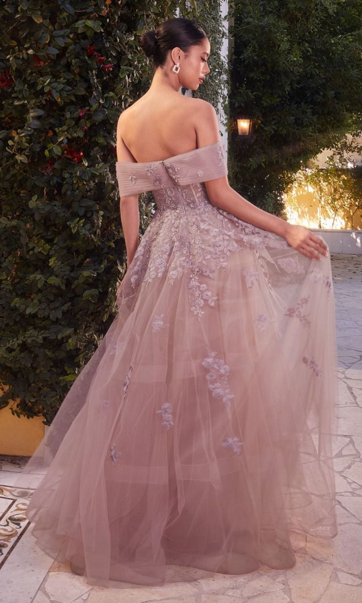 A woman stands outdoors on a stone path, holding part of her dress and facing away, wearing the Long Strapless Sweetheart A-Line Prom Dress A1348 in lavender tulle with floral embroidery.