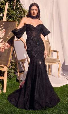 A woman wearing the Andrea & Leo A1354 long mermaid prom dress with sheer off-the-shoulder sleeves stands by a floral painting and a chair on a lawn, with white drapery in the background.