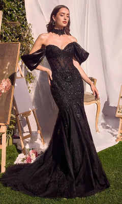 A woman poses outdoors among art easels and draped white fabric, wearing the Andrea & Leo A1354 long mermaid prom dress featuring a beaded evening gown with a sheer bodice and dramatic detached sleeves.