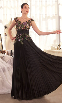 A woman poses indoors in the Andrea & Leo A1355 Sequin Long Pleated Prom Dress with floral appliques, standing near a dress form and sheer curtains in a bright room.
