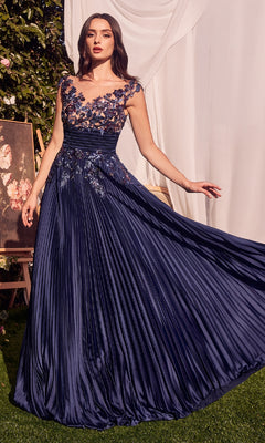 A woman poses outdoors in the Andrea & Leo A1355 Sequin Long Pleated Prom Dress, featuring sequin floral appliques on the bodice and shoulders, floor-length A-line silhouette, and extends one arm gracefully.