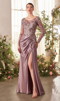 A woman wearing the Andrea and Leo A1403 long formal dress, featuring mauve satin with ruched skirt, floral lace bodice, sheer embroidered sleeves, and a thigh-high slit, stands indoors among floral arrangements.