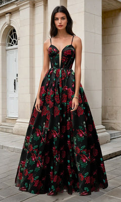 A woman stands outdoors in the Andrea & Leo A1465, a long black prom dress with red floral print, set against light stone walls and an arched doorway.