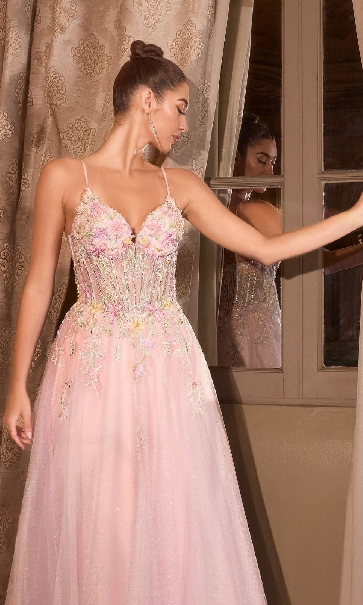 A woman in the Classic Long Pink Prom Dress: Andrea and Leo A1477, featuring embroidered flowers and an a-line silhouette, stands by a window holding the curtain aside, gazing to the left.