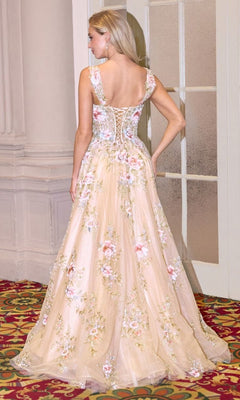 A woman stands indoors on a patterned carpet, facing away, wearing the Andrea and Leo A1480 Champagne Prom Ball Gown with floral embroidery and a lace-up back.