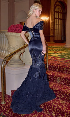 A woman in the Andrea and Leo A1482 long navy satin prom dress with an off-the-shoulder neckline and lace-up back stands on a red carpeted staircase, facing away from the camera.