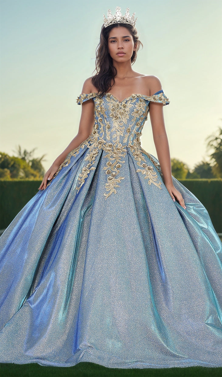 A woman in the Quinceanera Dress 1504 by Dancing Queen, an off-shoulder sparkling blue A-line gown with gold embellishments and a lace embroidered bodice, wears a crown and stands outdoors against a blurred background.