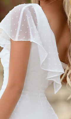 Close-up of a woman in the Ace White Graduation Dress, featuring one flutter sleeve and sheer details, showing part of her back and blonde hair.