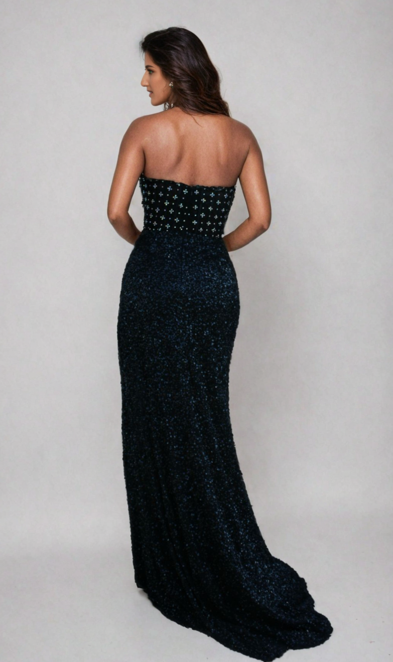 A woman stands with her back to the camera, wearing the Aleta Strapless Beaded Designer Prom Dress 1278—a floor-length black gown with a fitted, decorated bodice and textured beaded skirt.