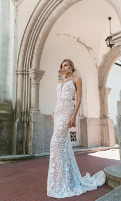 A woman stands outdoors before stone arches, wearing the Long White Lace Formal Dress: Tina Holly BB008, featuring a fitted silhouette with floral lace patterns and sheer design.
