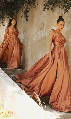 Two women wear Shoulder-Tie Long Satin V-Neck Prom Dress BD105 in copper as they walk down outdoor concrete steps next to a textured beige wall with overhanging greenery.