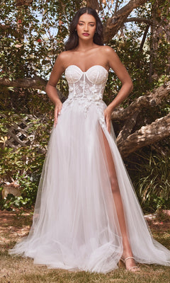 A woman stands outdoors among trees in the Puff-Sleeve Off-White Long Prom Dress CB080W, featuring a sheer bodice, floral appliqué, high slit, and sheer puff sleeves.