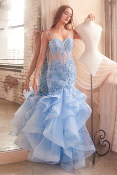 A woman in the Ladivine CC8915 Long Ruffle Mermaid Prom Dress stands beside a dress form in a softly lit room with exposed brick walls and a large window.