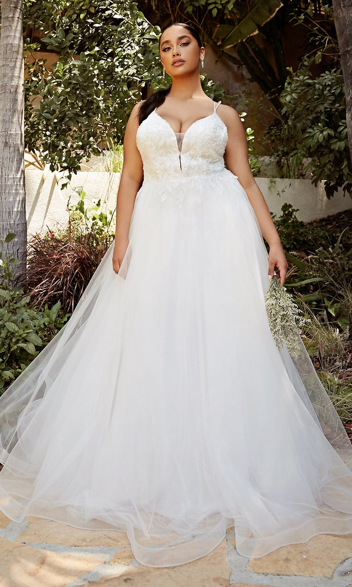 A woman stands outdoors holding a bouquet, wearing the Off-White Long A-Line Wedding Dress CD0154W, featuring a sleeveless design and floral lace bodice.