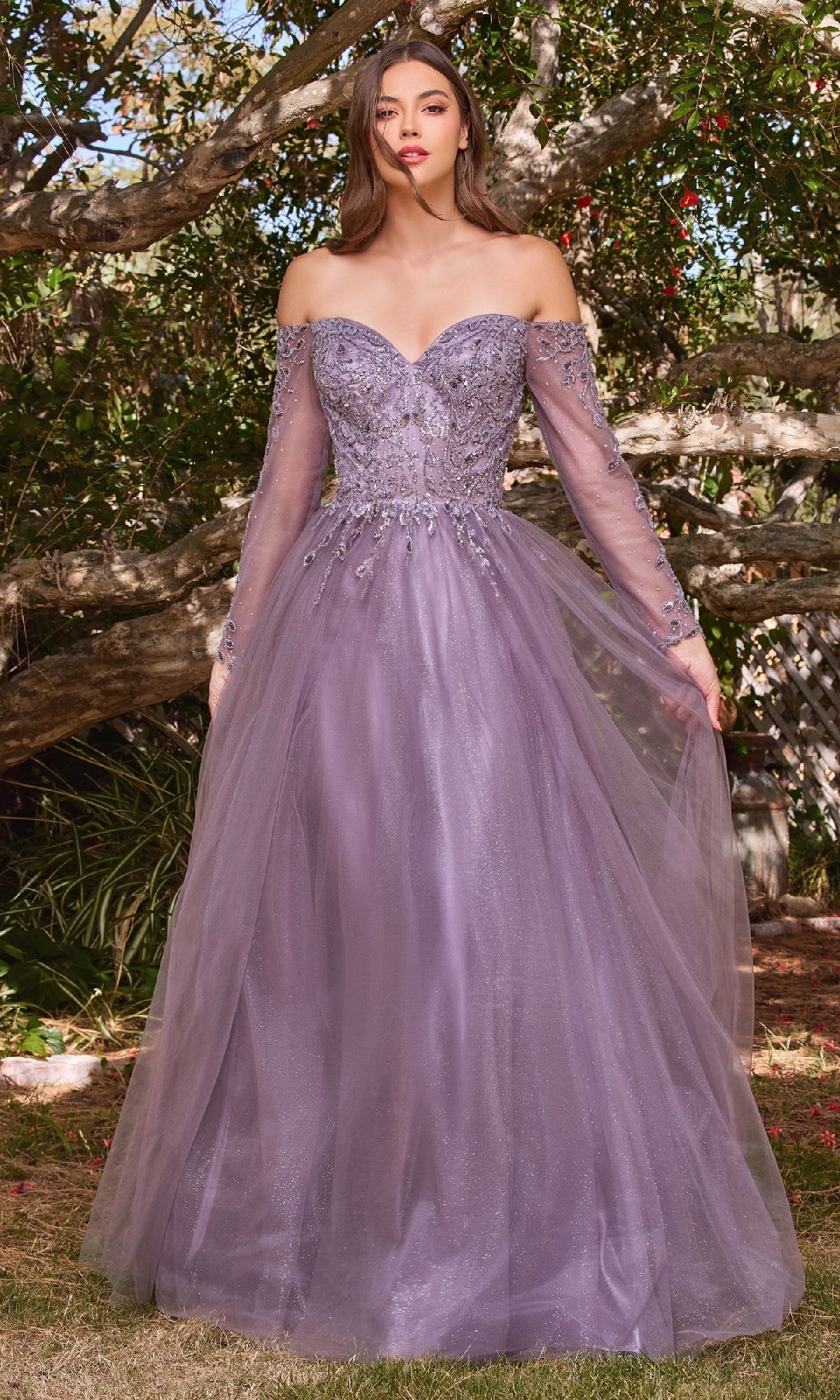 A woman stands outdoors in front of trees wearing the Ladivine CD0172, a lavender off-the-shoulder prom dress with sheer long sleeves and a beaded bodice.