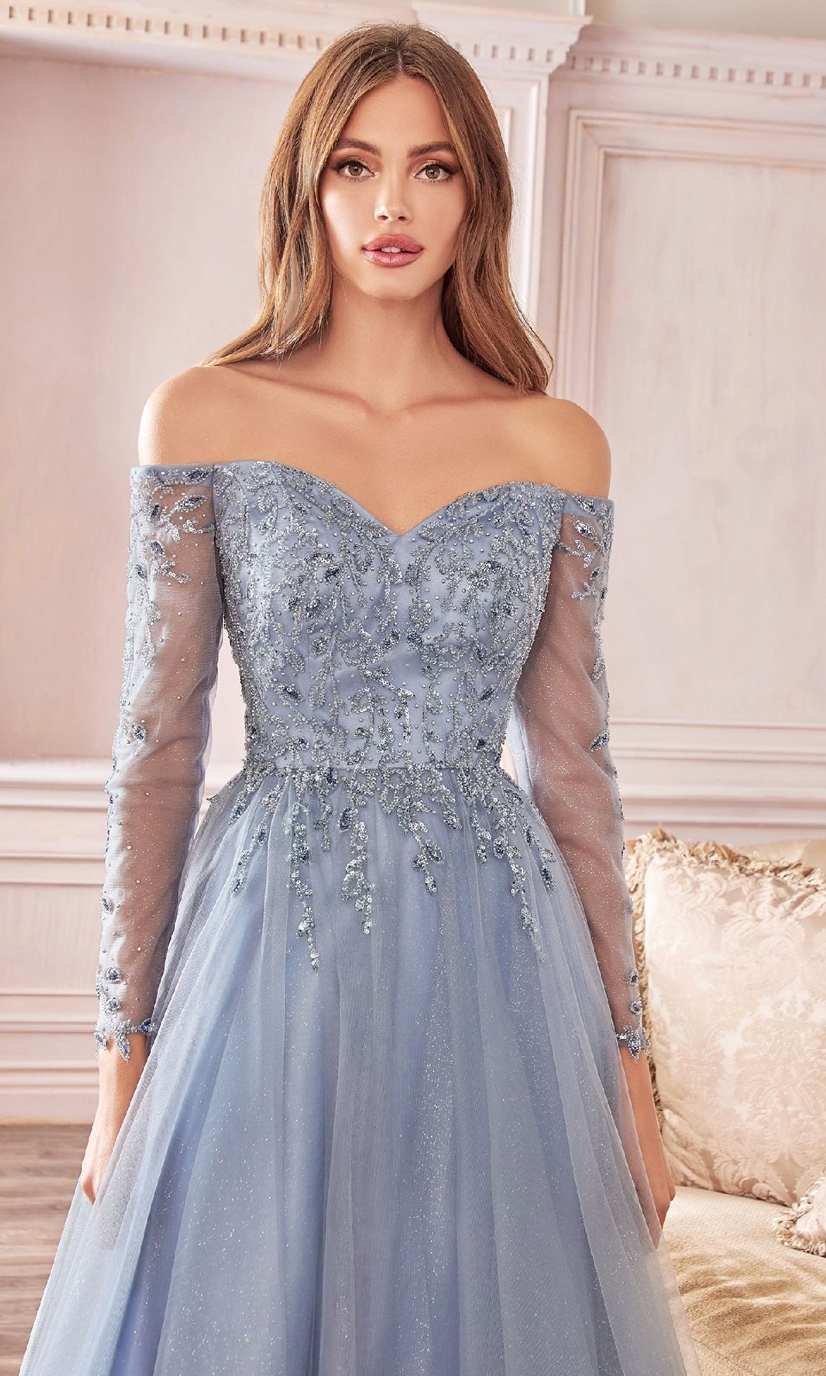 A woman stands indoors against an elegant backdrop, wearing the Ladivine CD0172—an off-the-shoulder long prom dress with long sleeves, light blue sheer fabric, and delicate floral embroidery.