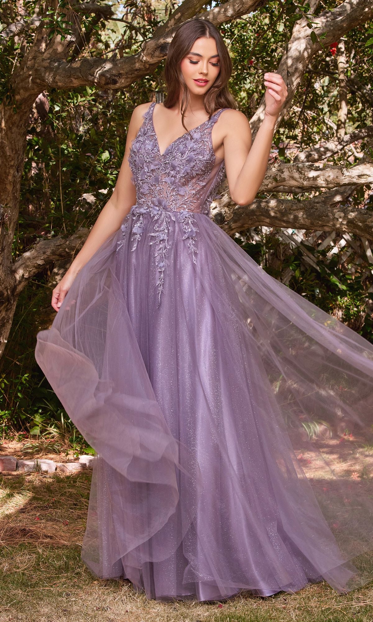 A woman stands outdoors in the Glitter Tulle Illusion Prom Dress: Ladivine CD0181, a long lavender gown with floral embroidery and a dreamy tulle skirt. She is surrounded by trees and lush greenery.