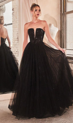 A woman stands indoors near a window and mirror, wearing the Lace-Up Strapless Long Glitter Prom Dress CD0217 featuring a floor-length black gown with a deep neckline and full tulle skirt.